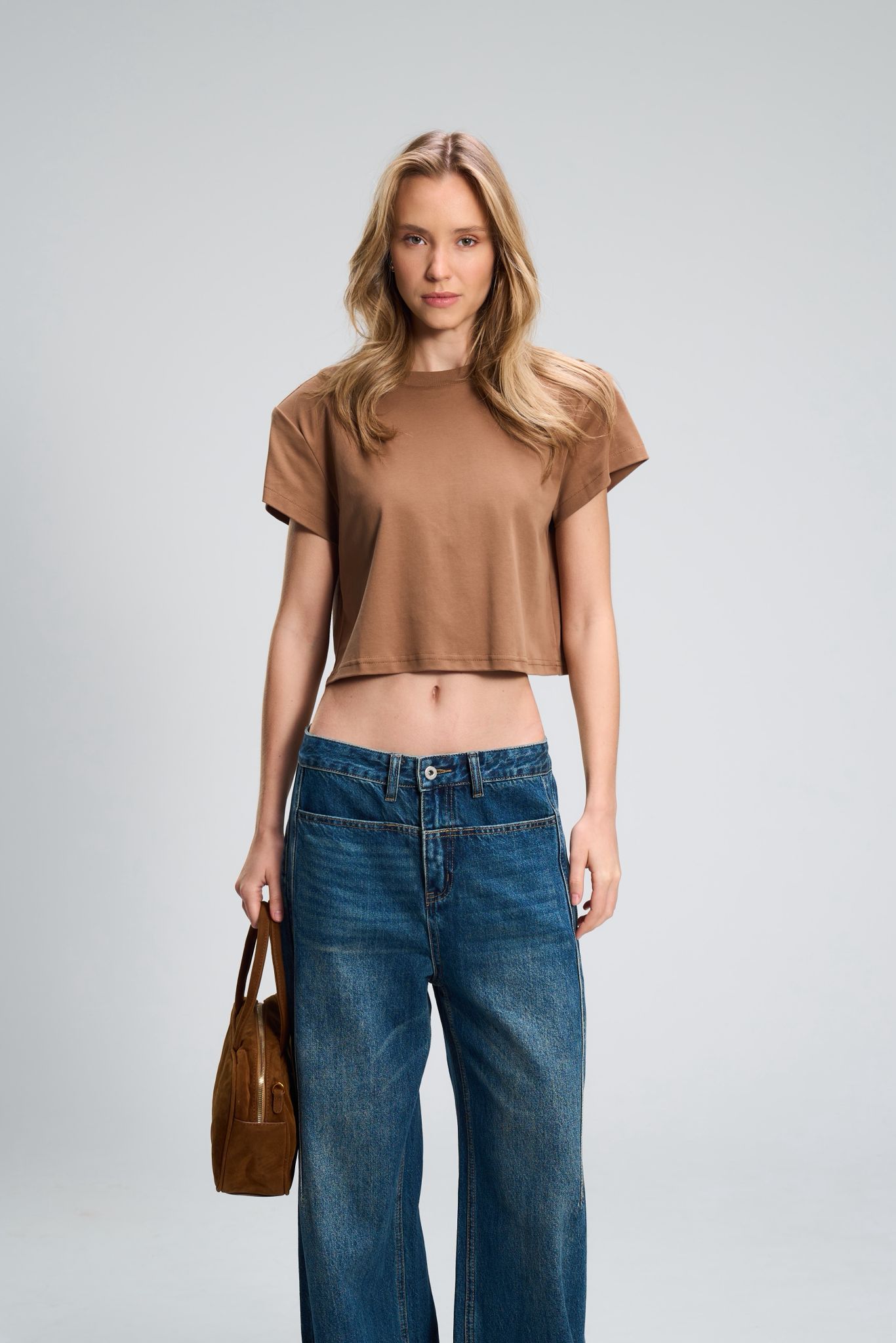 מכנס ג’ינס לארי אישה לובשת חולצת קרופ רחבה וג'ינס בגזרה רחבה, מחזיקה תיק.